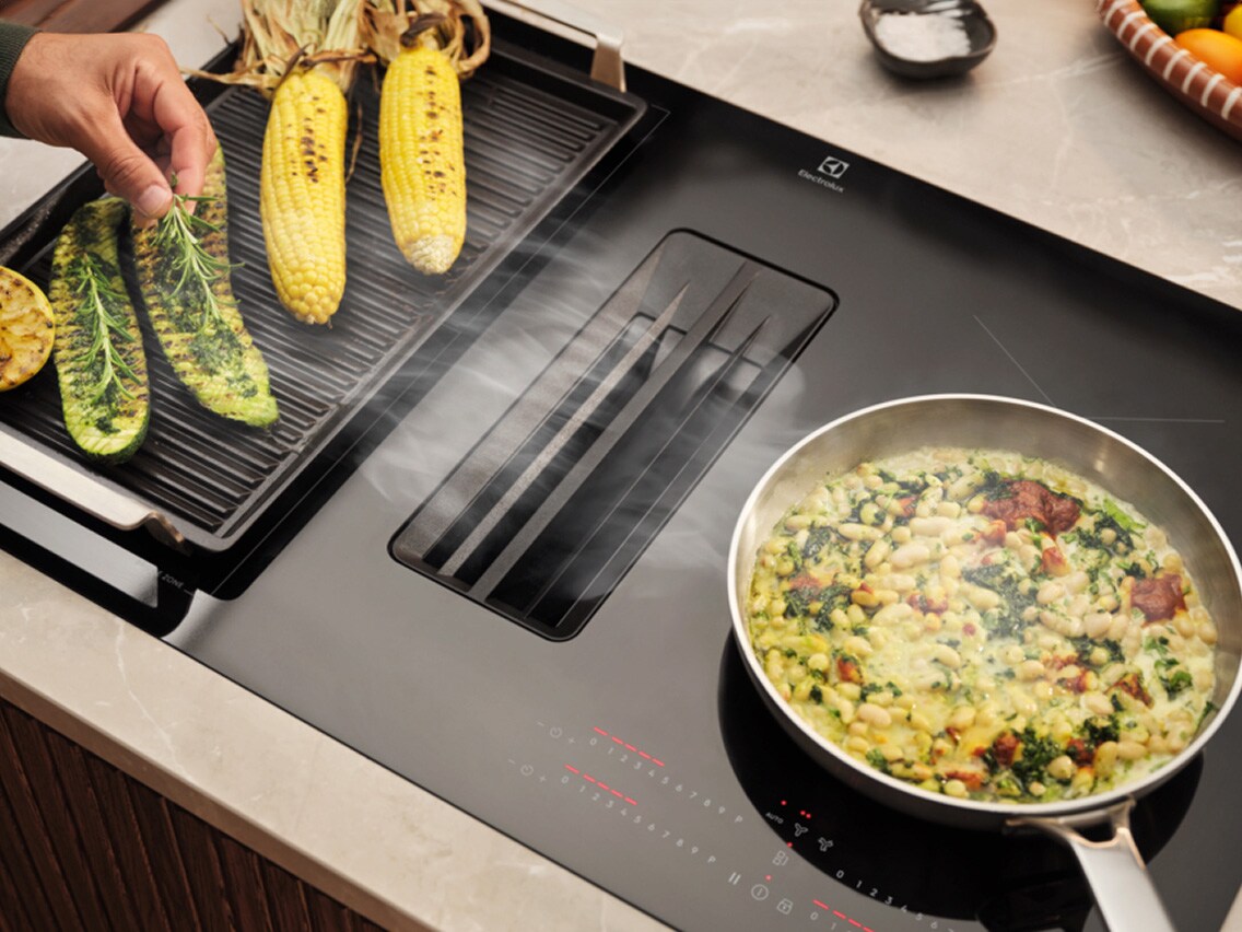 Zoom sur la table de cuisson Electrolux avec hotte intégrée, plancha et casserole