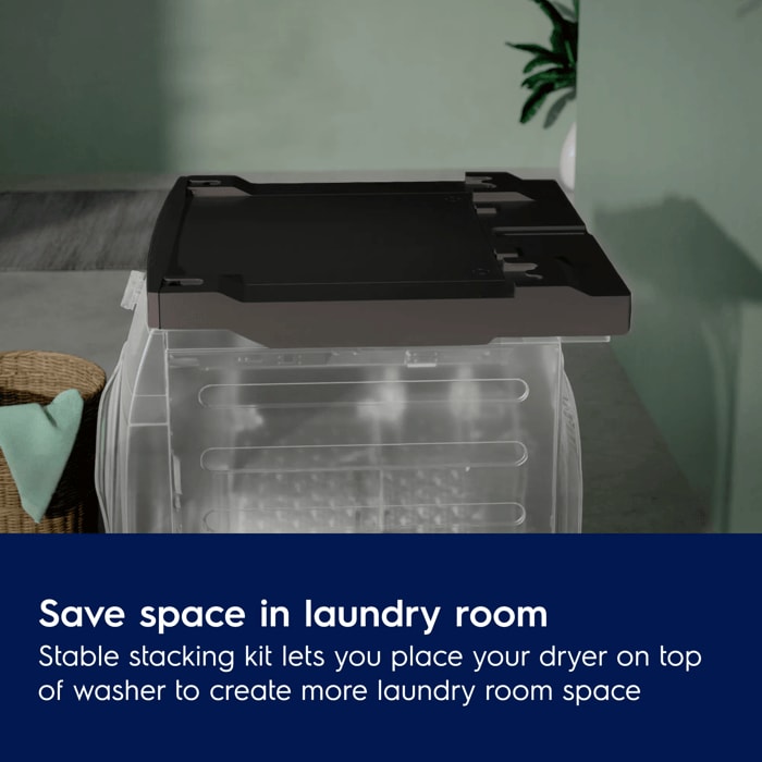A dark gray stacking kit installed on top of a transparent washing machine model in a laundry room setting.